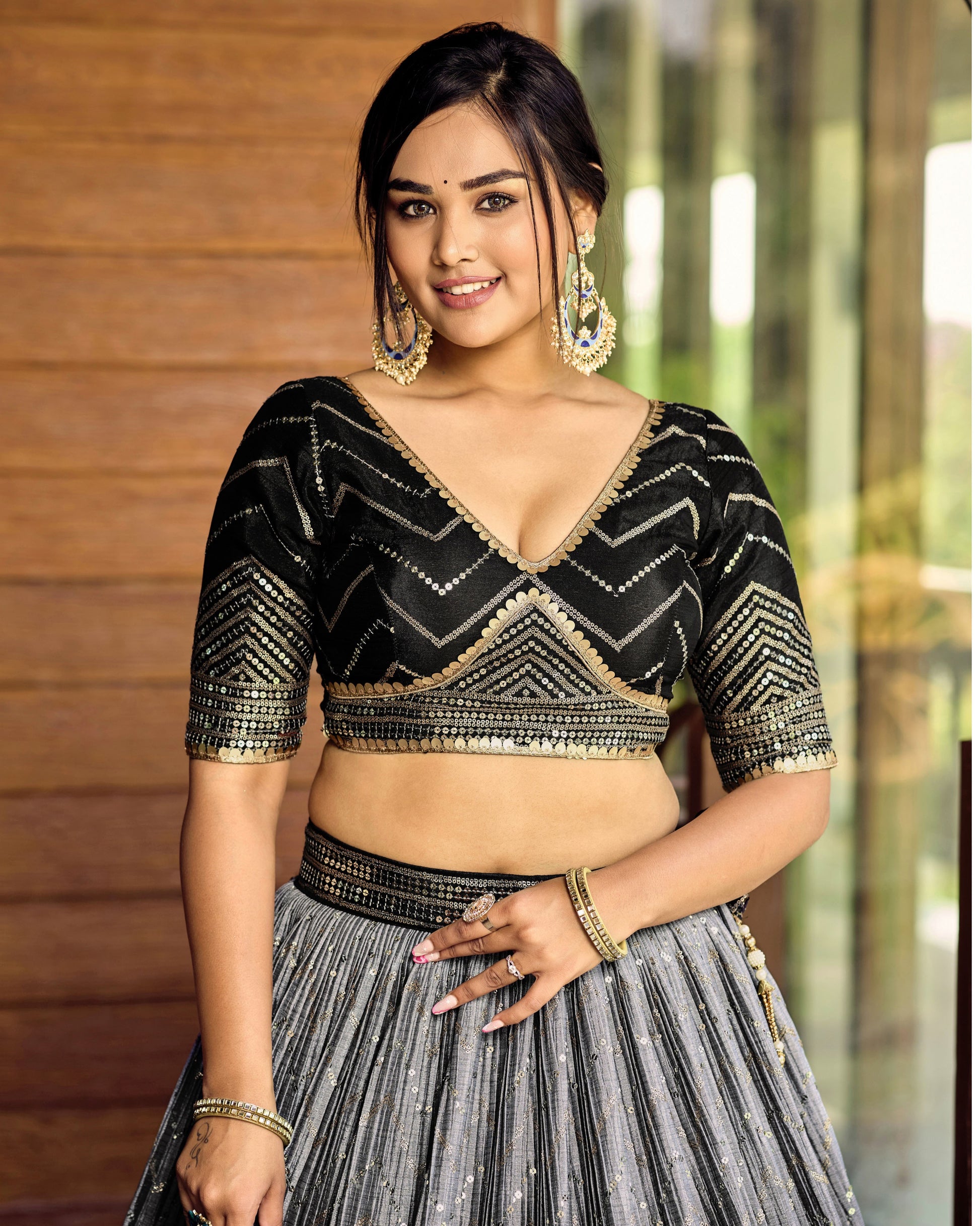Woman wearing a black and gold blouse with a gray pleated skirt indoors.