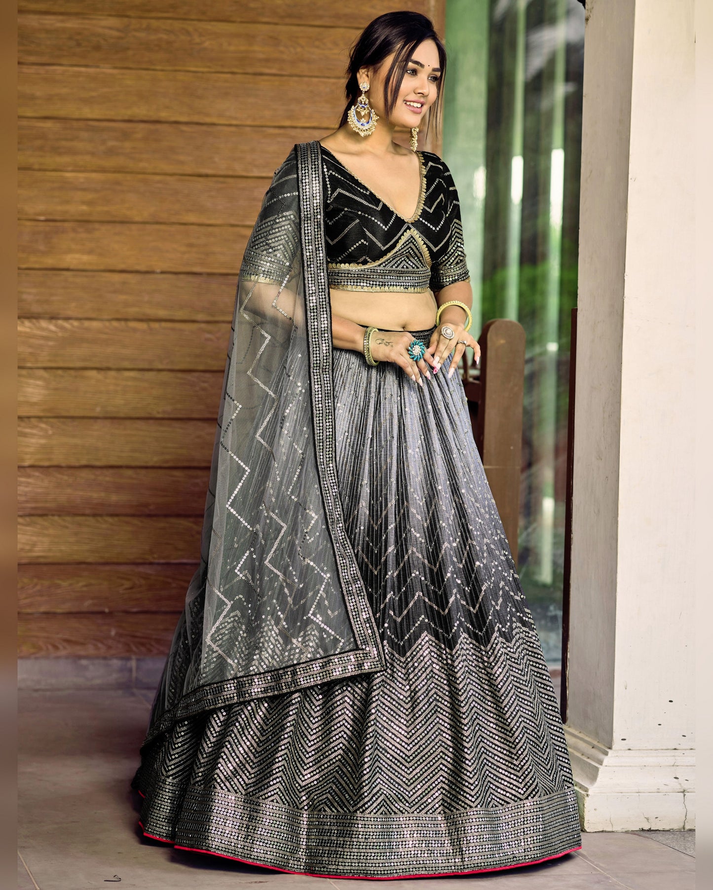 Woman wearing a traditional black and gray saree with a wooden wall background
