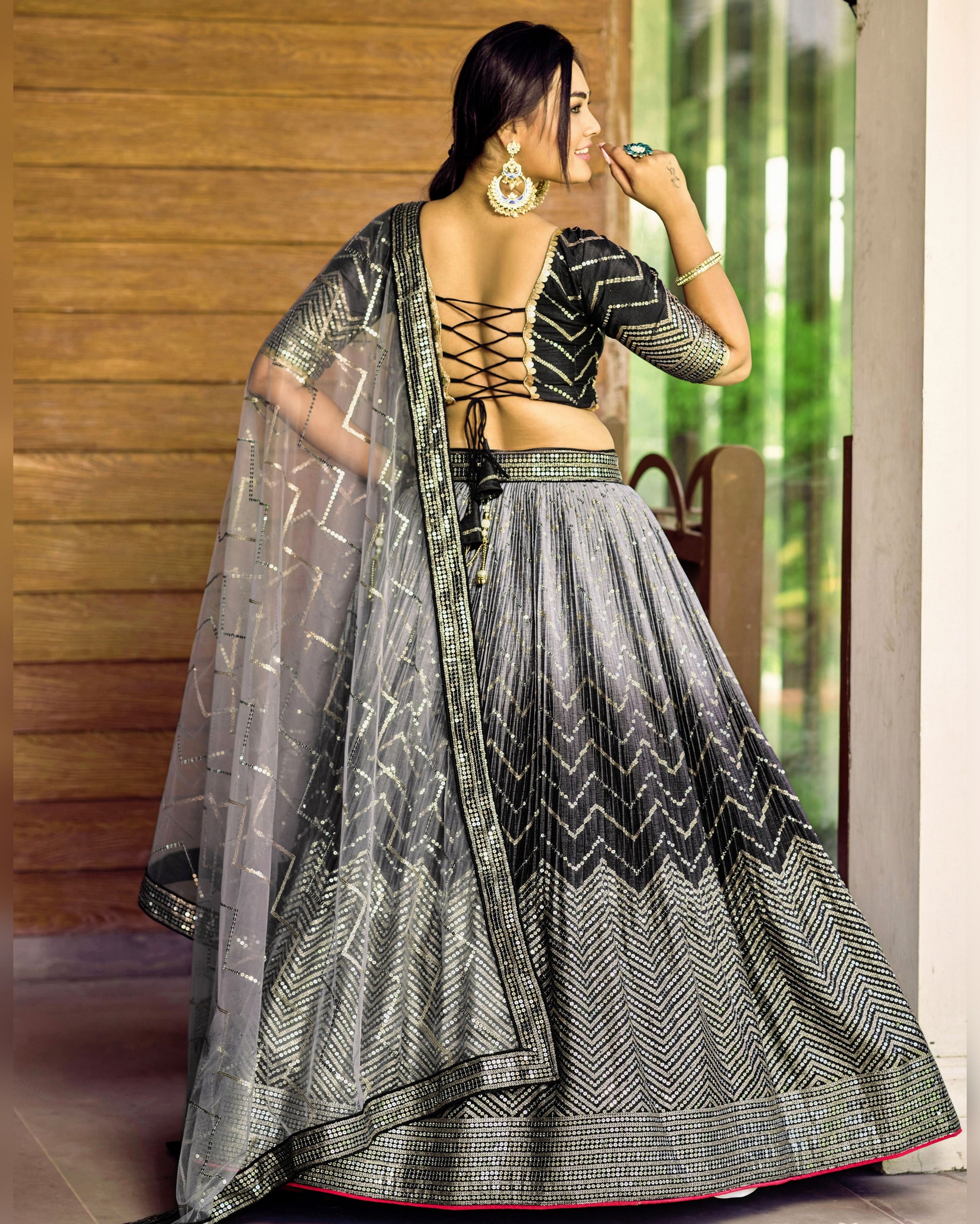 Woman wearing a black and white patterned saree with a wooden wall and greenery in the background