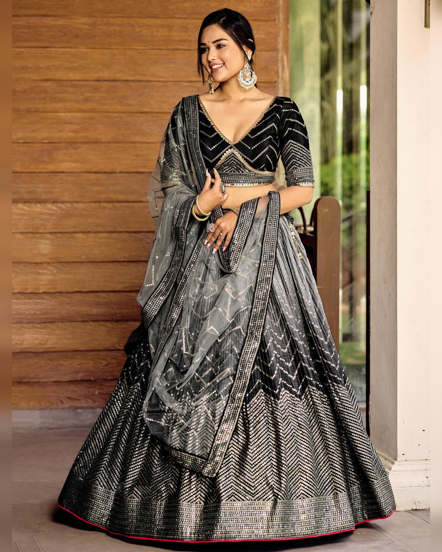 Woman wearing a black and gray patterned saree with a wooden wall background