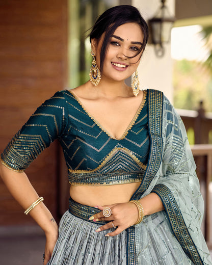 Woman wearing a traditional outfit with a blue blouse and light gray saree, smiling outdoors.