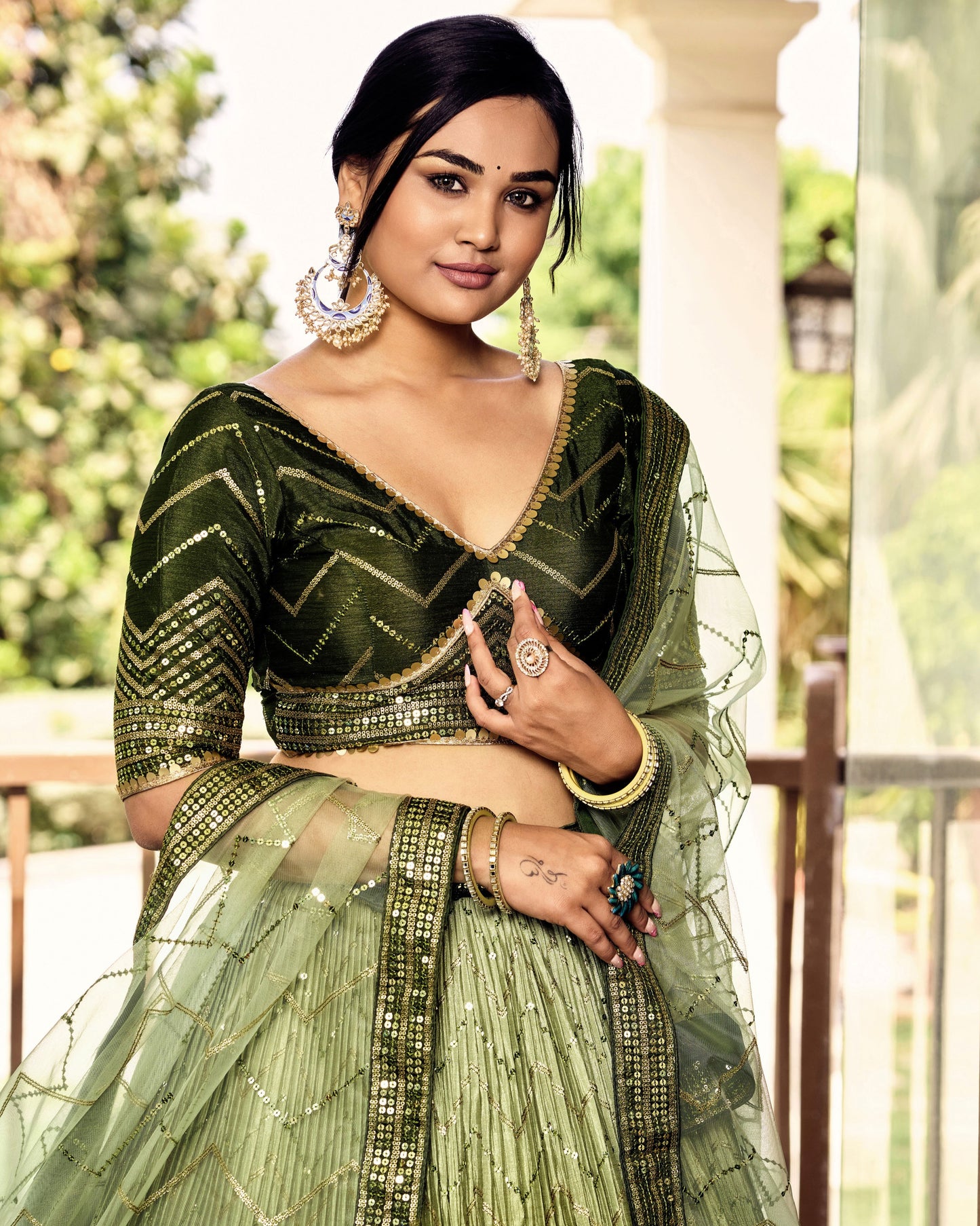 Woman in a green traditional outfit with intricate designs outdoors.