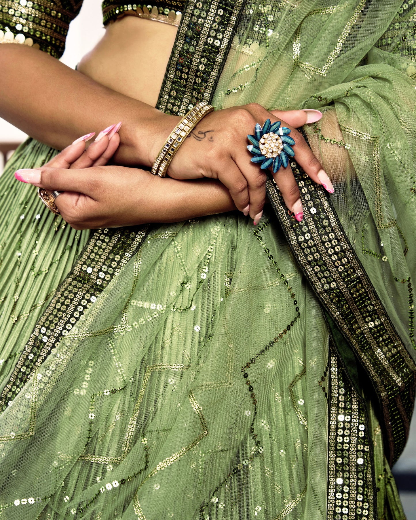 Close-up of a person wearing a green saree with gold details and a blue ring.