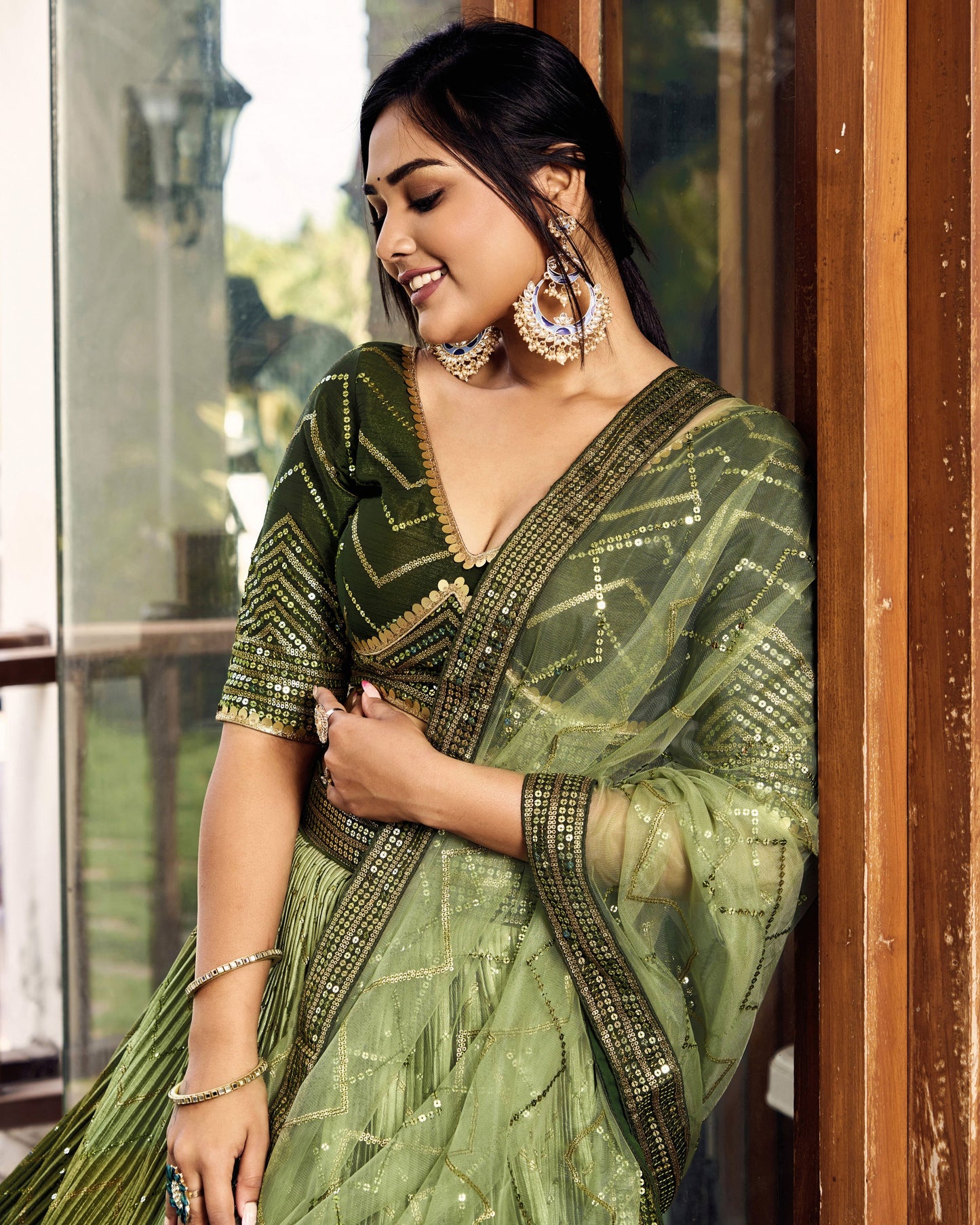 Woman wearing a green saree with gold details indoors.