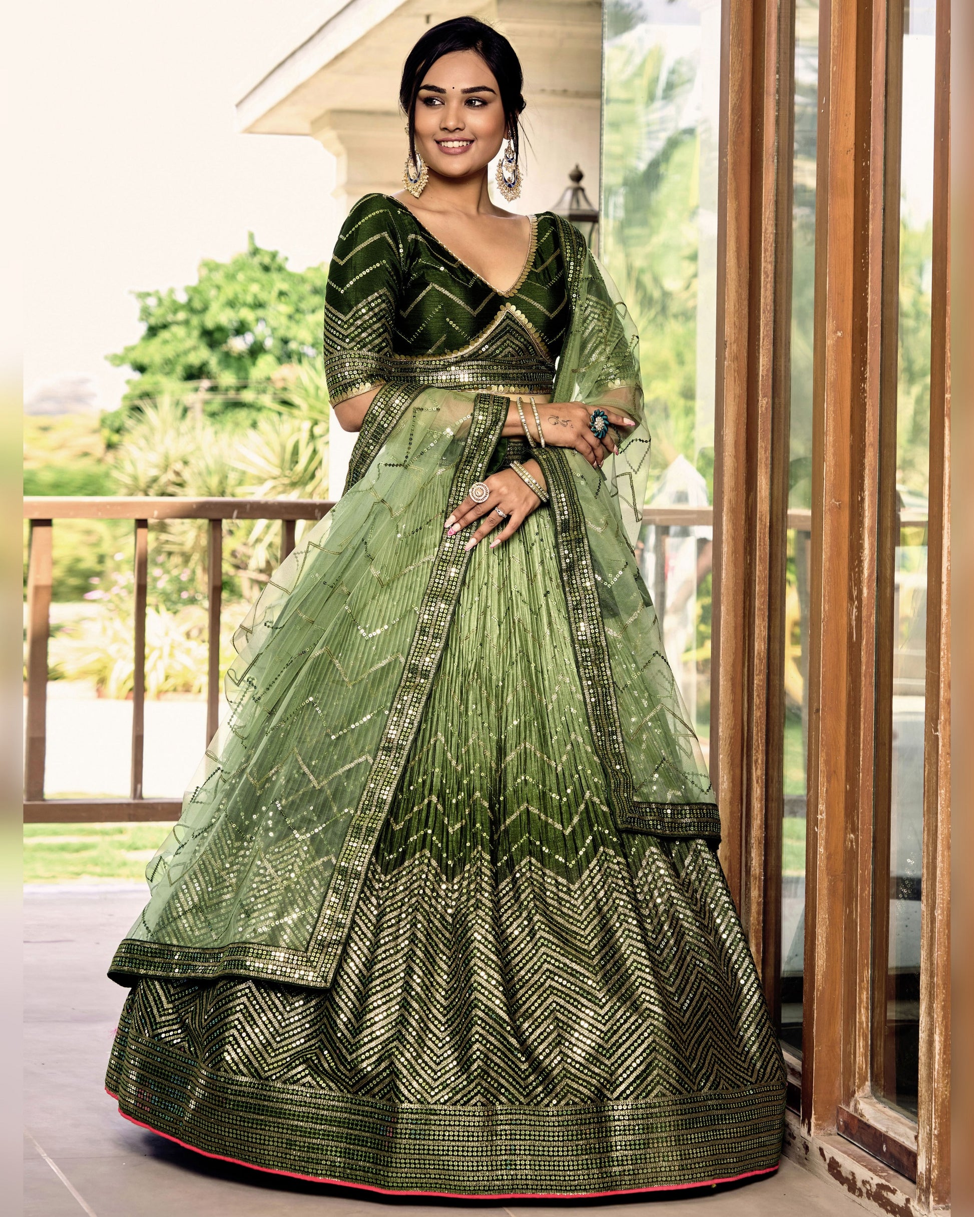 Woman wearing a green traditional outfit with intricate patterns in an outdoor setting.