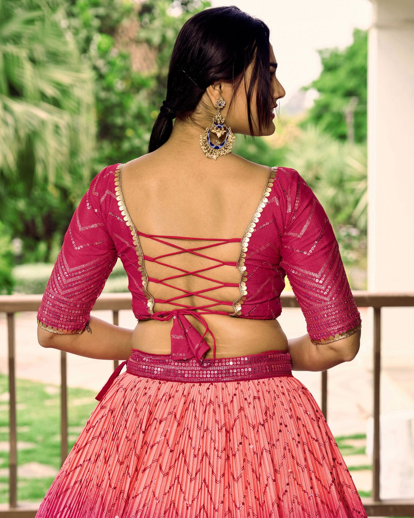 Woman wearing a pink traditional outfit with a backless design, standing outdoors.