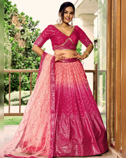 Woman wearing a pink and red traditional outfit with a gradient effect, standing outdoors.