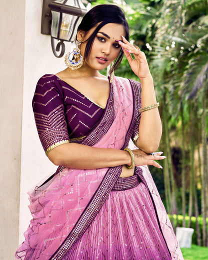 Woman in a pink and purple saree with jewelry, standing outdoors.