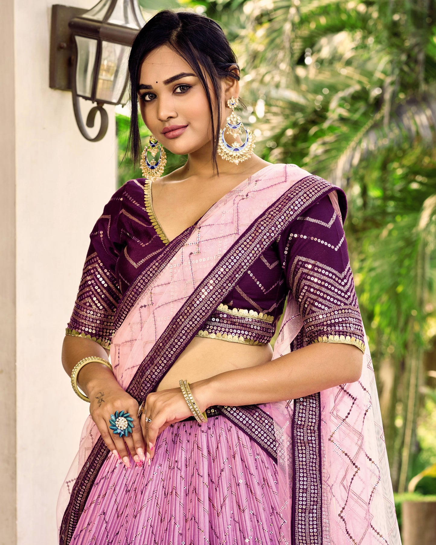 Woman wearing a pink and purple saree with jewelry outdoors