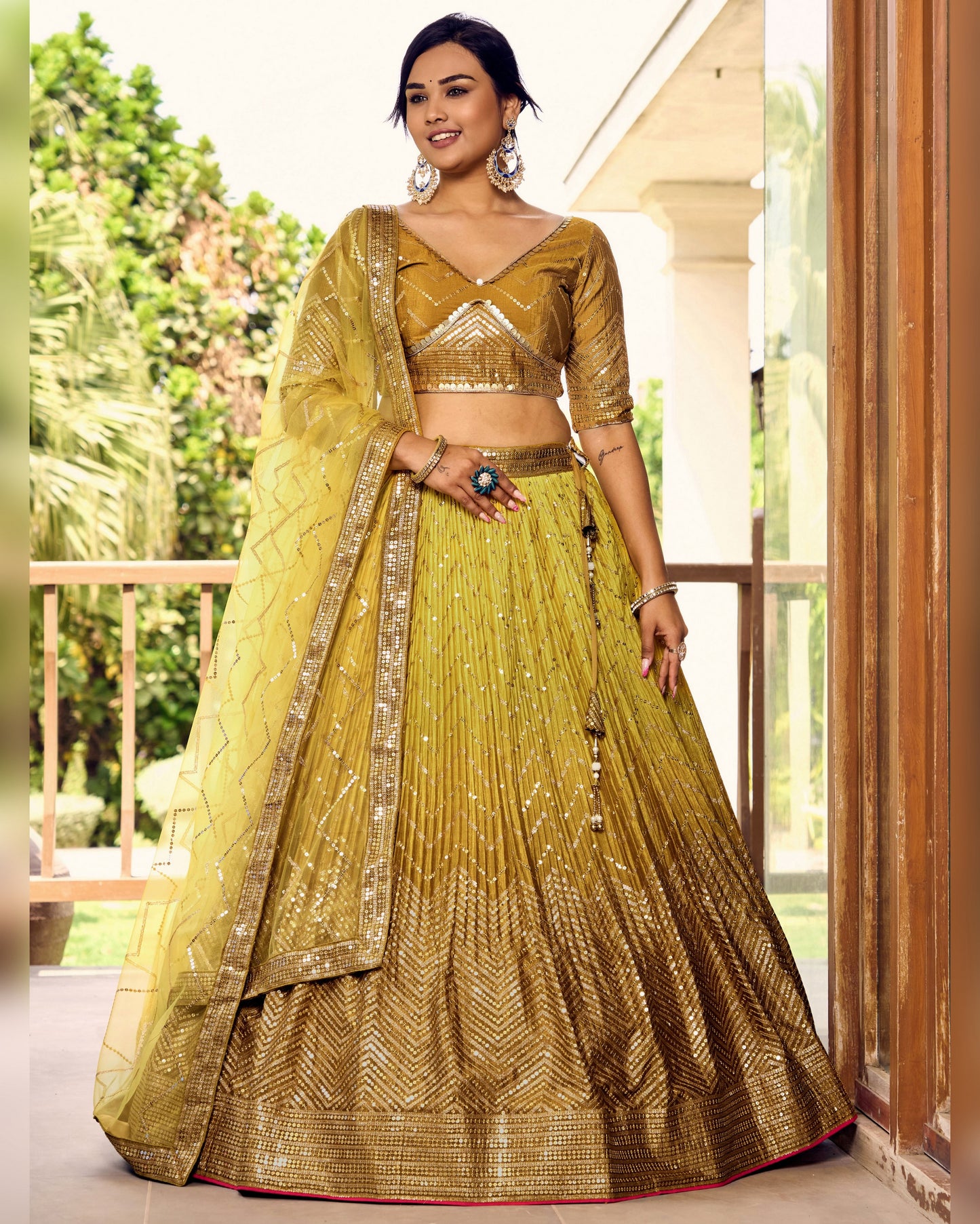 Woman wearing a traditional yellow and gold outfit with a matching dupatta, standing outdoors.