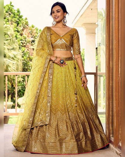 Woman wearing a traditional yellow and gold outfit with a matching dupatta, standing outdoors.