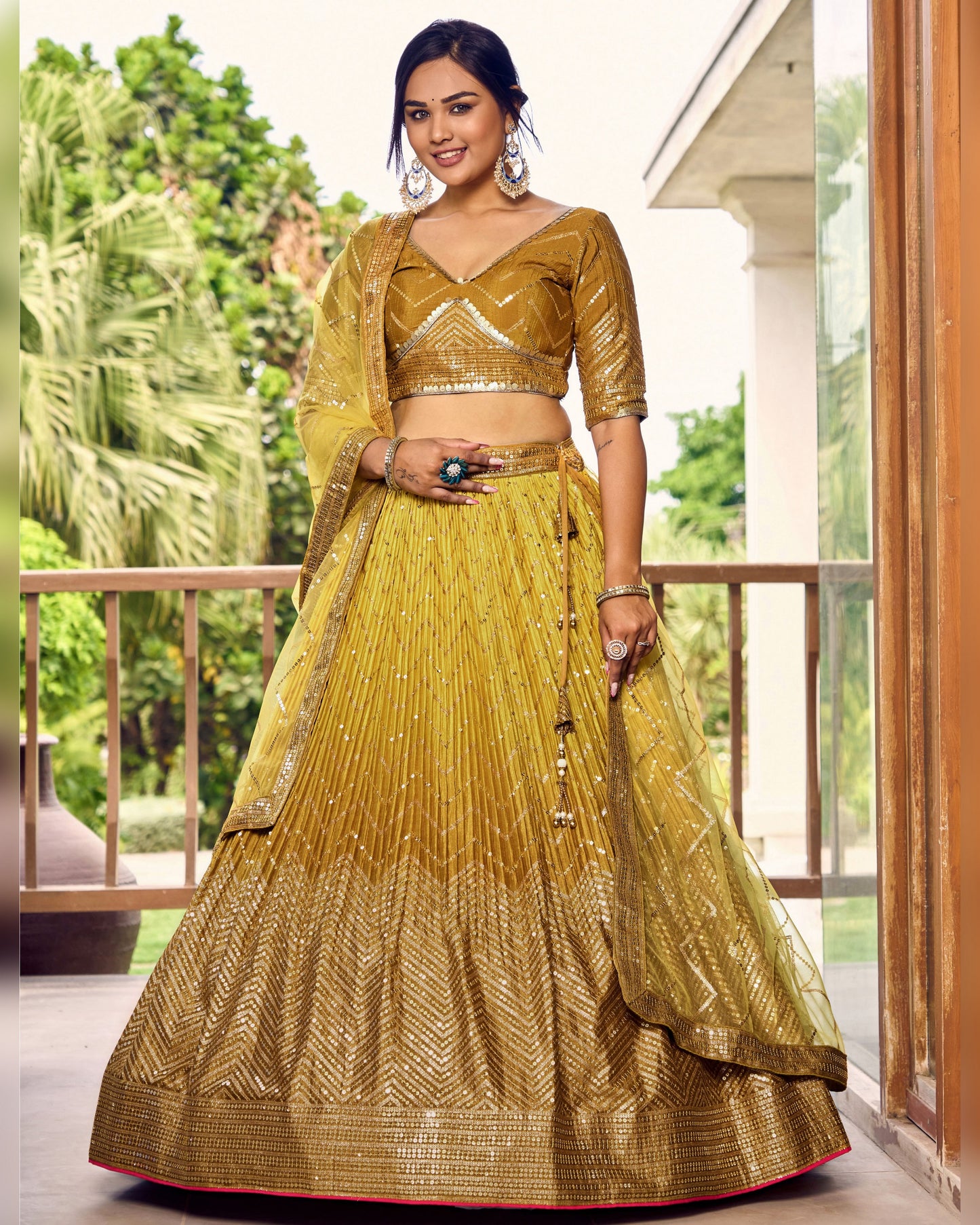 Woman wearing a mustard yellow traditional outfit standing on a balcony with greenery in the background