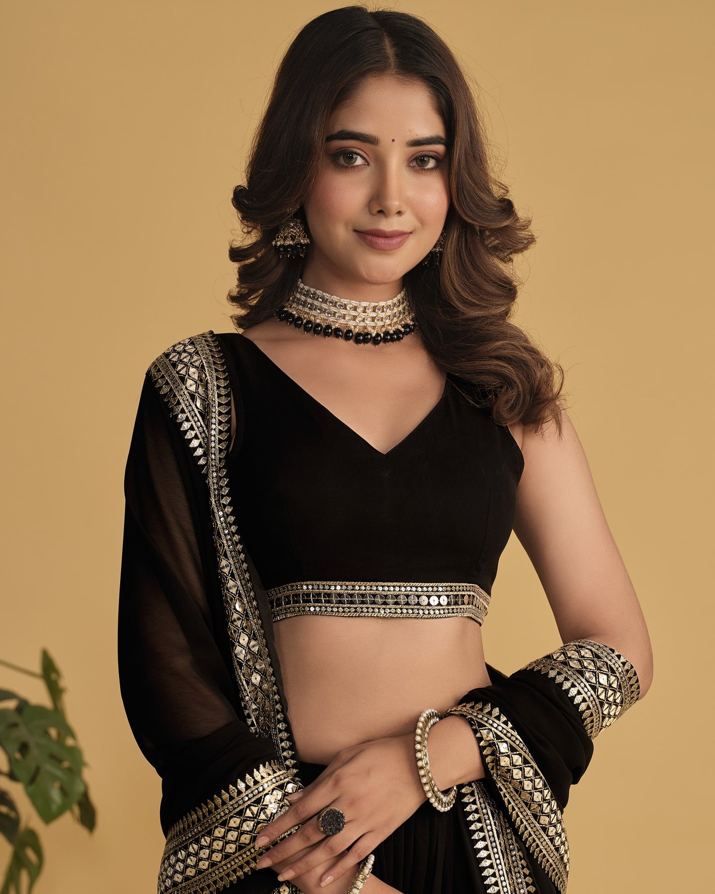Woman wearing a black saree with gold embroidery on a beige background