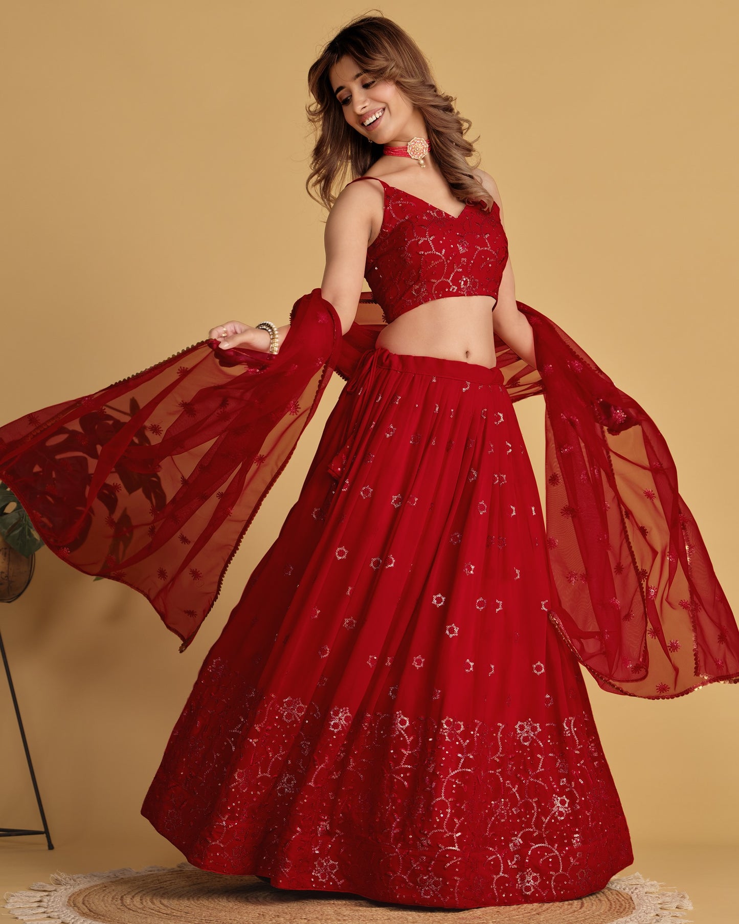 Woman wearing a red embroidered lehenga with a sheer dupatta against a beige background