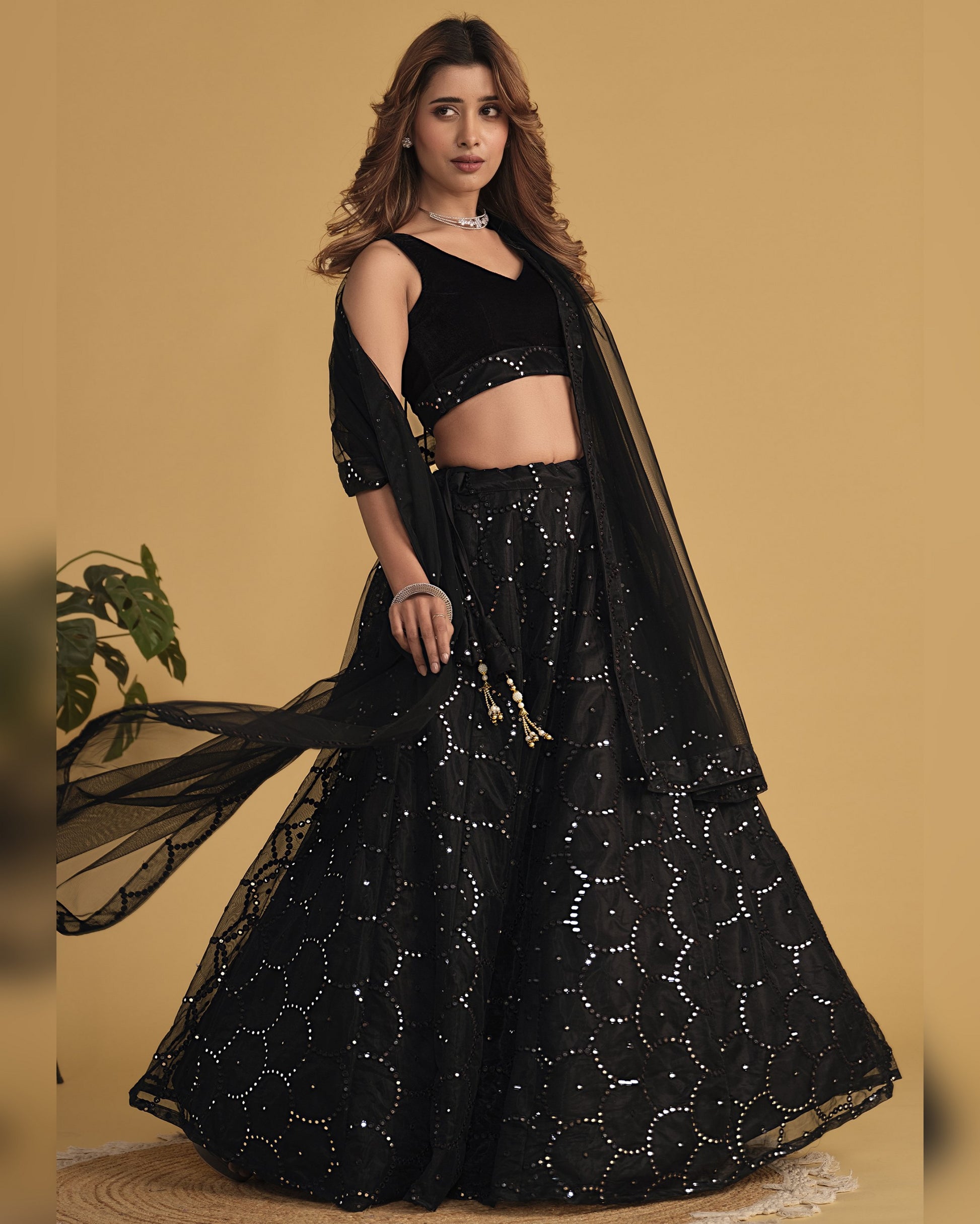 Woman wearing a black embroidered lehenga with a sheer dupatta against a beige background