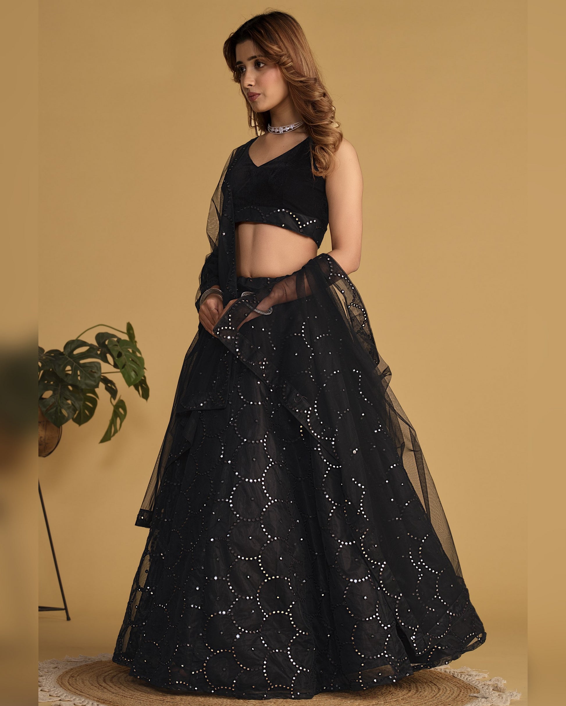 Woman wearing a black embroidered lehenga with a matching top against a beige background