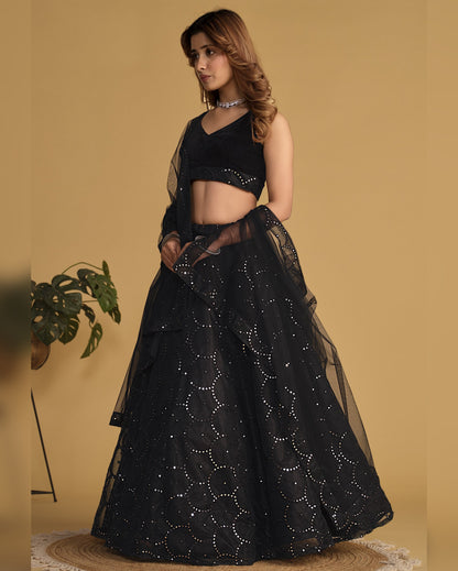 Woman wearing a black embroidered lehenga with a matching top against a beige background