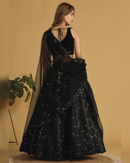 Woman wearing a black embroidered traditional outfit with sheer sleeves against a beige background