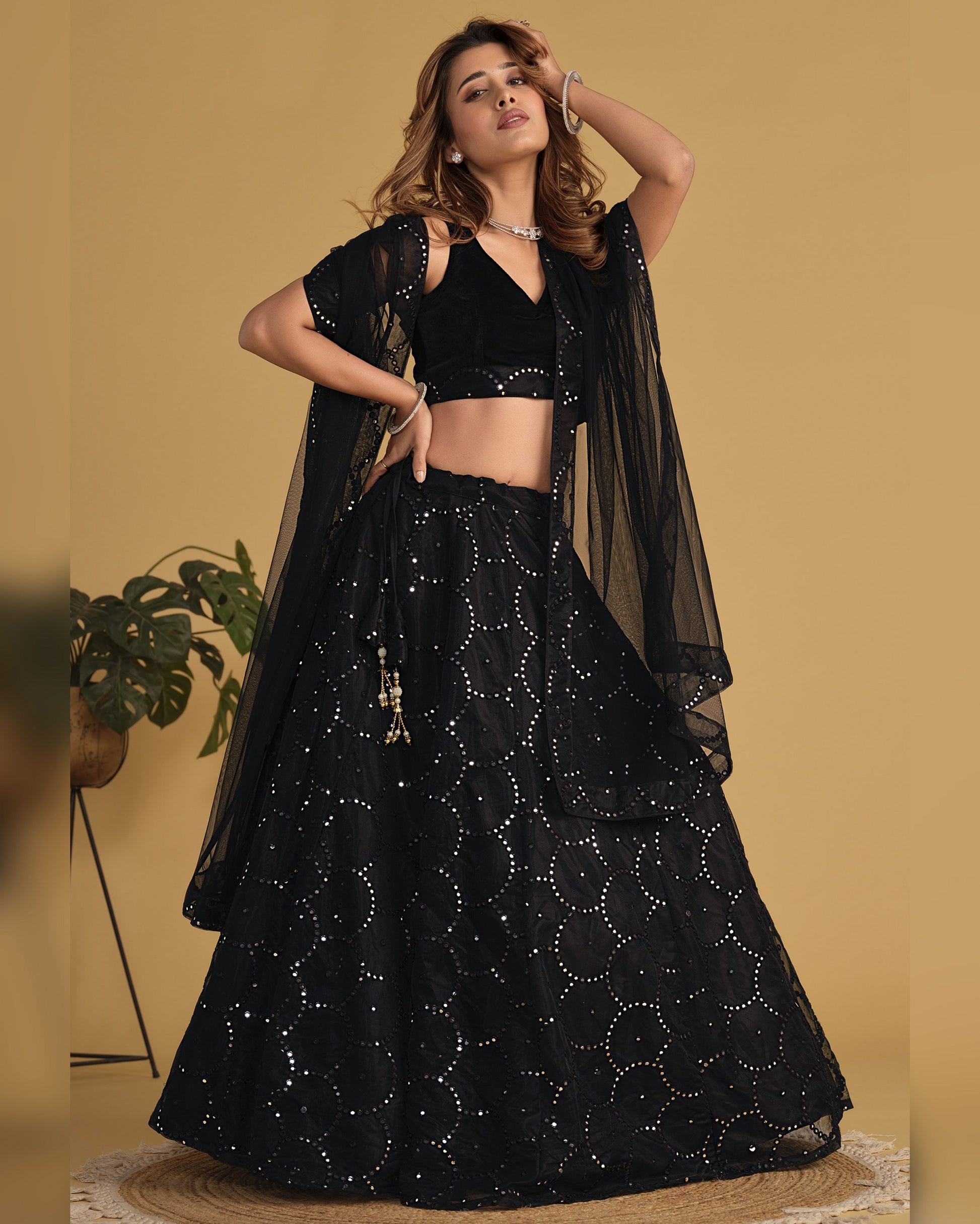 Woman wearing a black traditional outfit with a sheer dupatta against a beige background