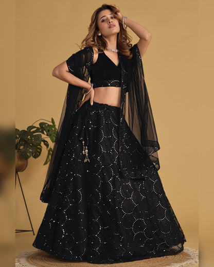 Woman wearing a black traditional outfit with a sheer dupatta against a beige background