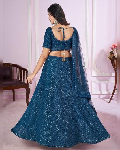Woman wearing a blue traditional outfit in a room with pink walls and a wooden chair.