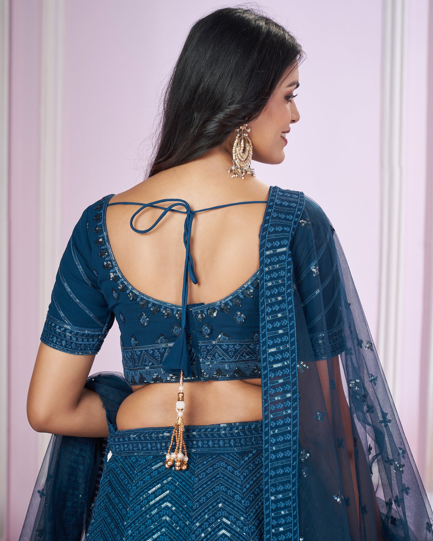 Woman wearing a blue traditional outfit with a sheer dupatta against a light pink background