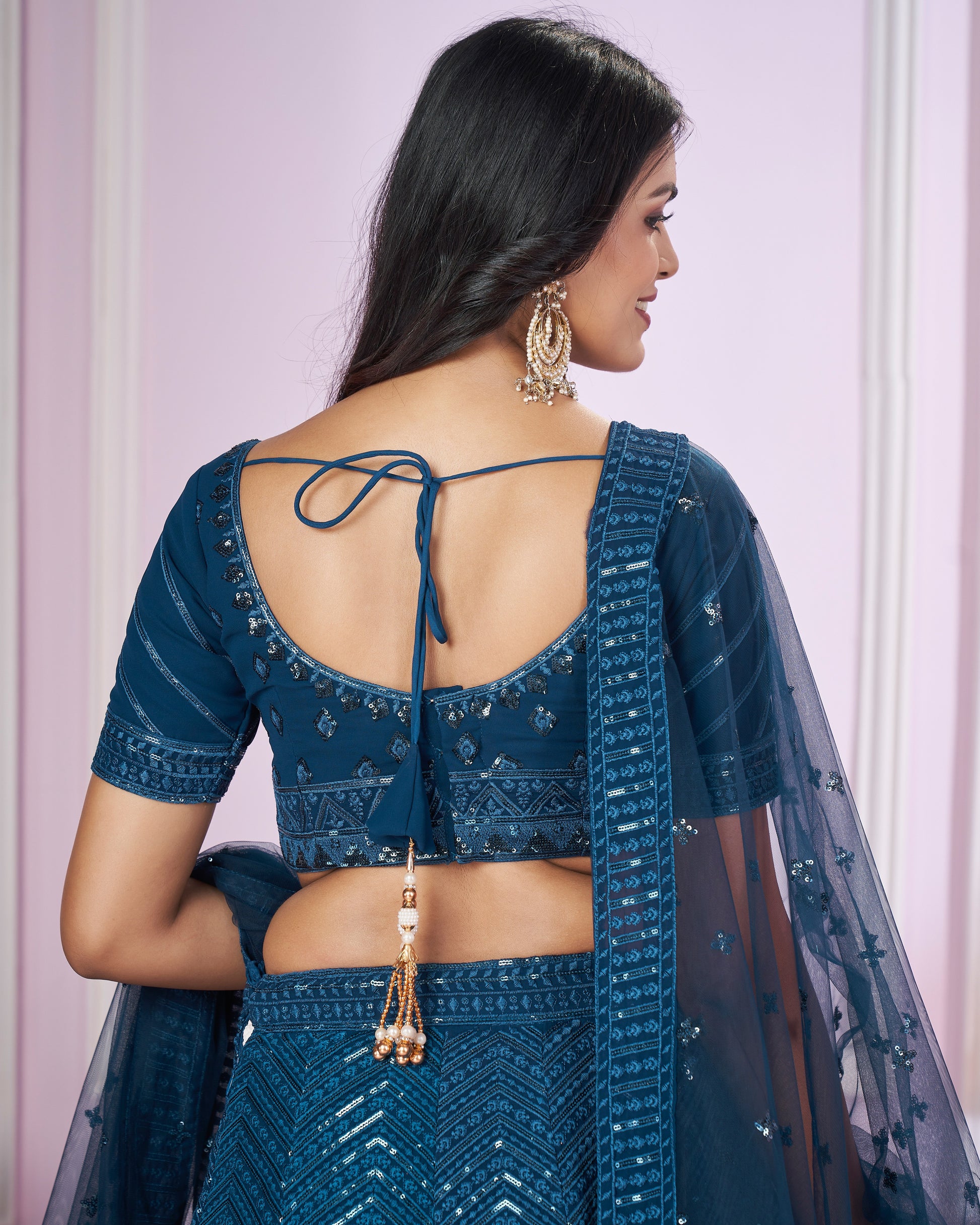 Woman wearing a blue traditional outfit with a sheer dupatta against a light pink background