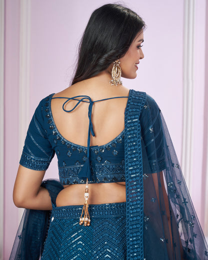 Woman wearing a blue traditional outfit with a sheer dupatta against a light pink background