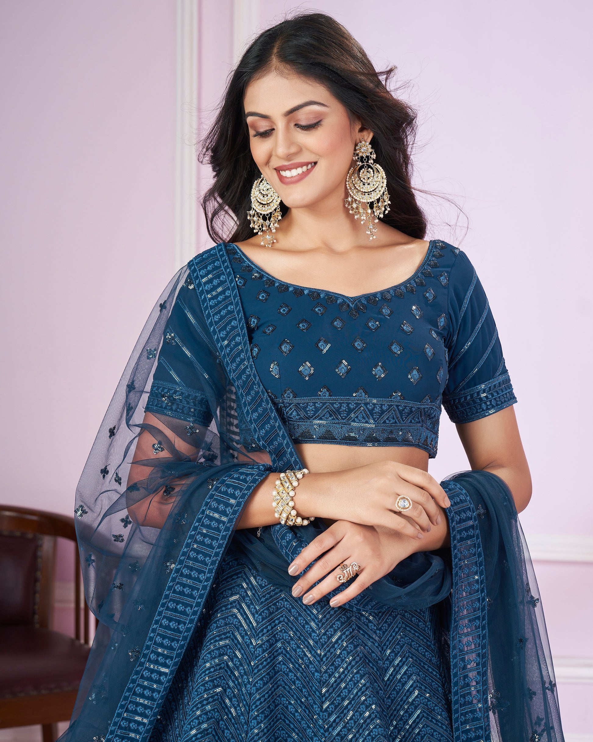 Woman wearing a blue saree with a matching blouse, posing against a light pink wall.