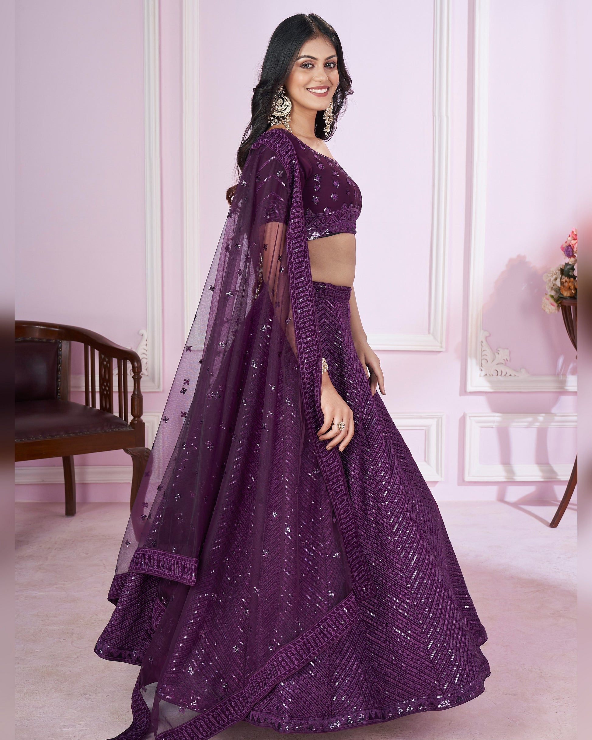 Woman wearing a purple traditional outfit with a matching dupatta in an elegant room.