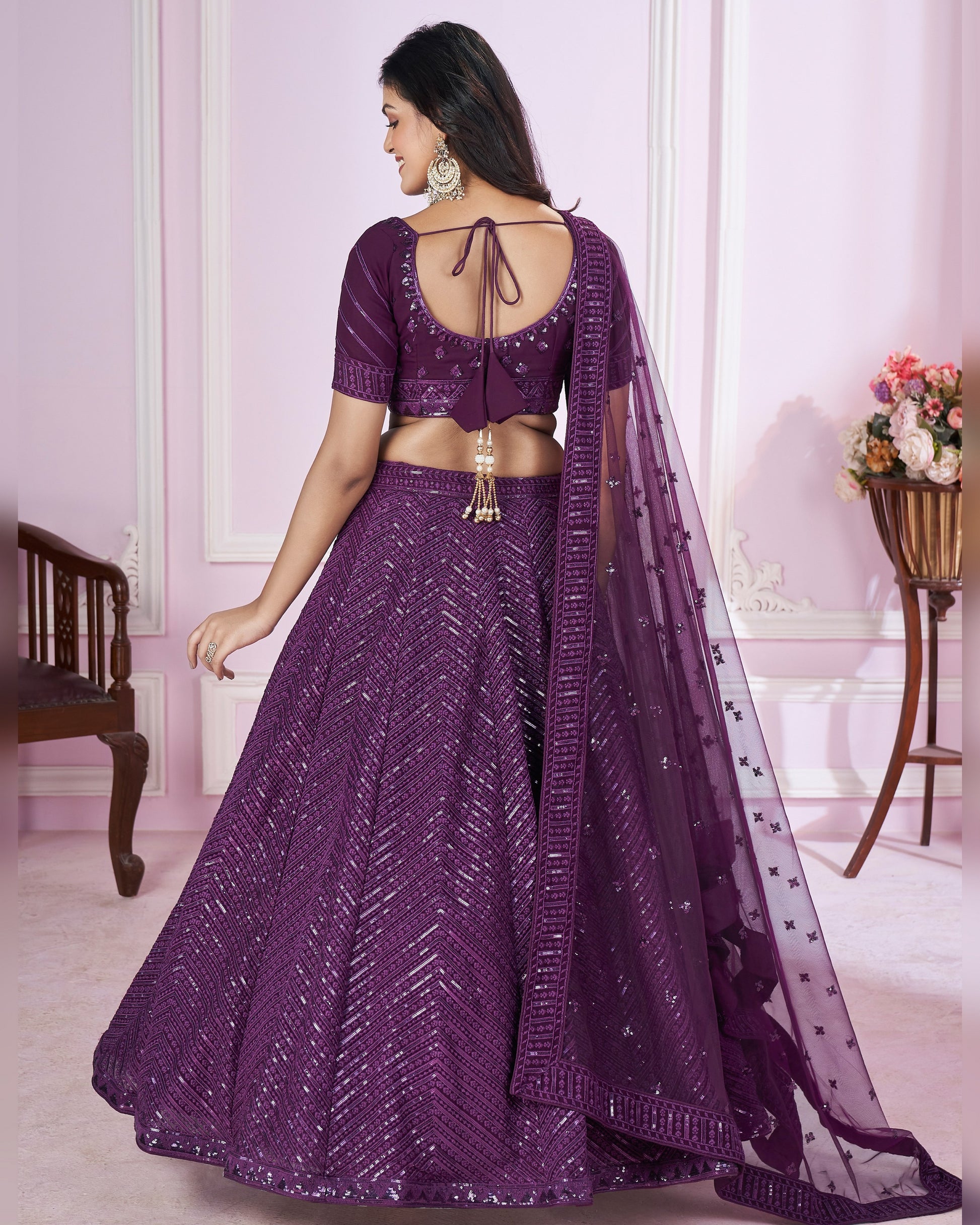 Woman wearing a purple traditional outfit with a matching dupatta in a well-lit room.