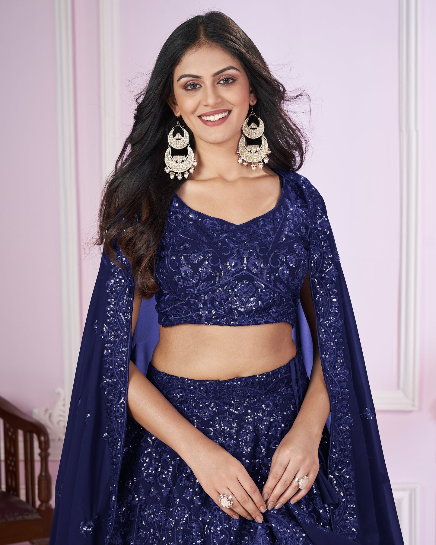 Woman wearing a blue traditional outfit with a matching dupatta against a light pink wall.