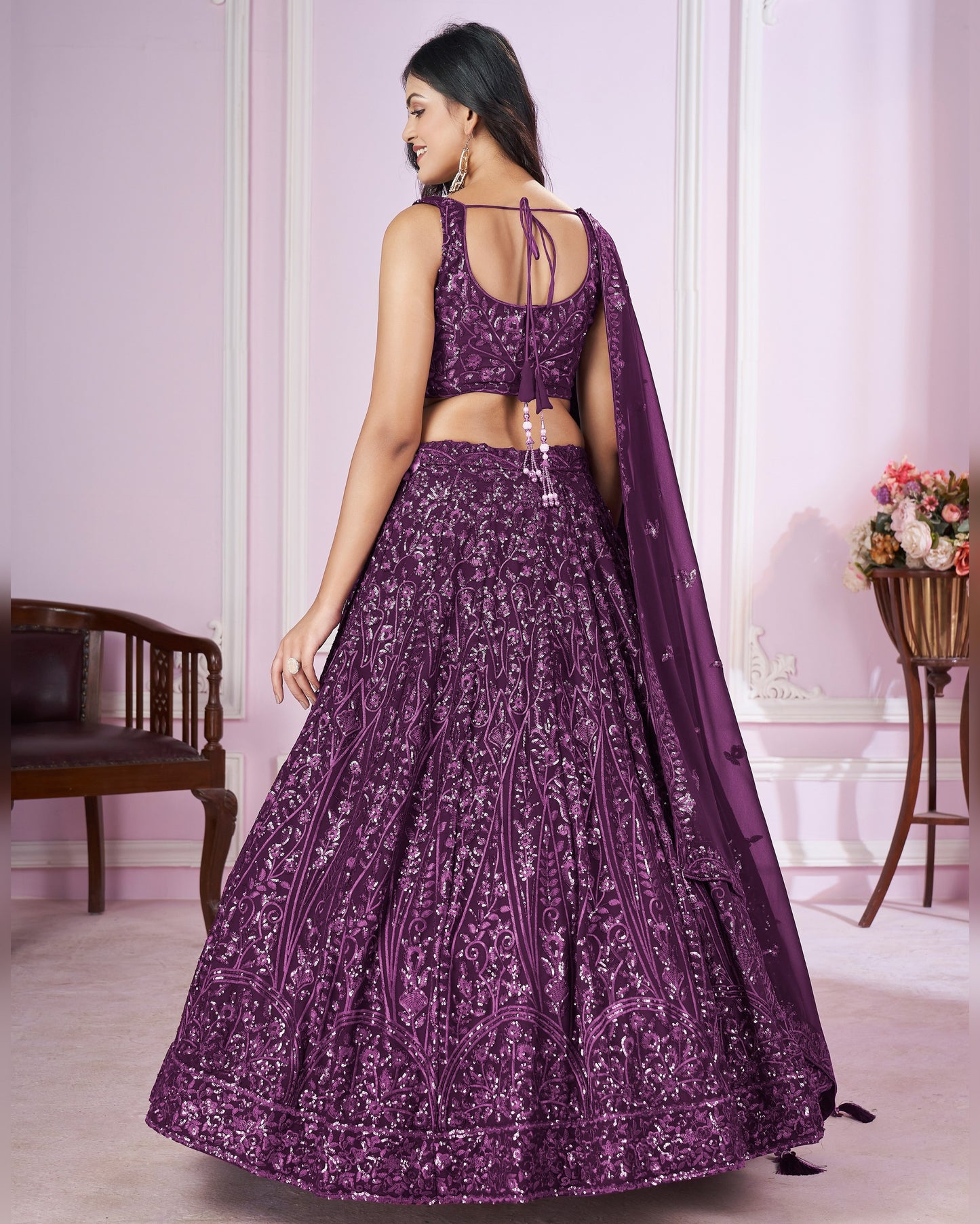 Woman wearing a purple embroidered lehenga in a room with a floral arrangement.