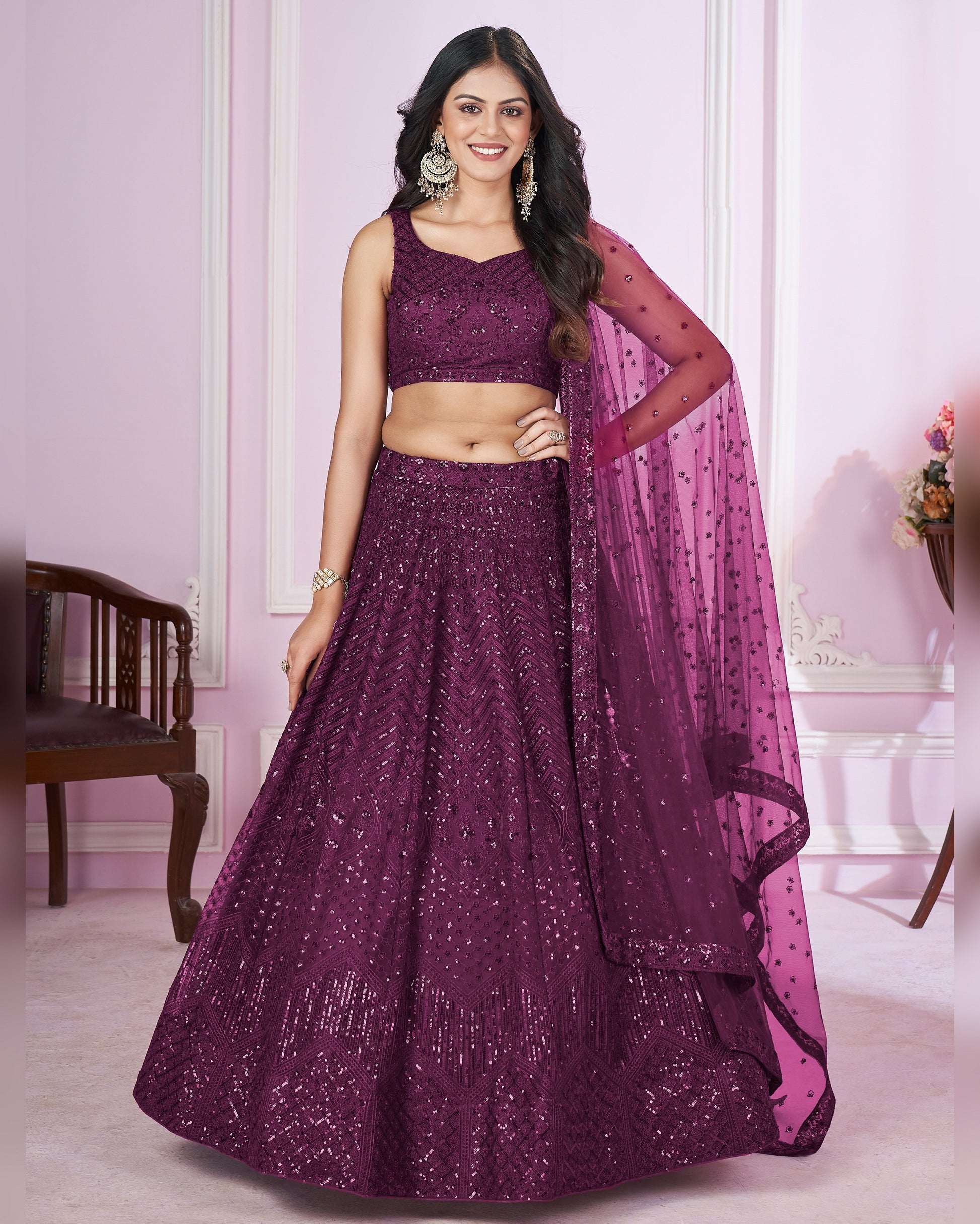 Woman wearing a purple traditional outfit with a pink dupatta in a well-lit room.