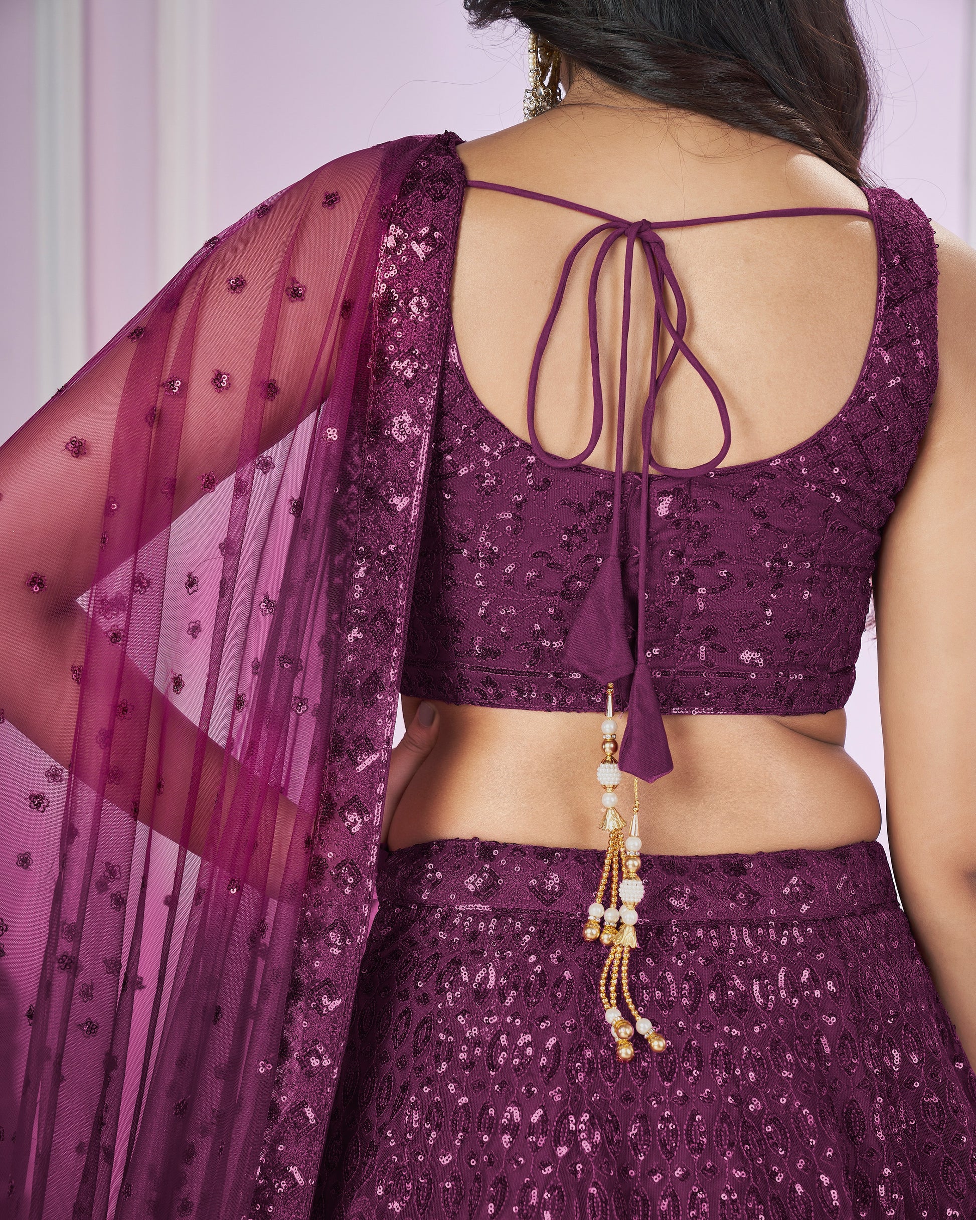 Purple traditional outfit with a sheer dupatta and decorative jewelry on a plain background