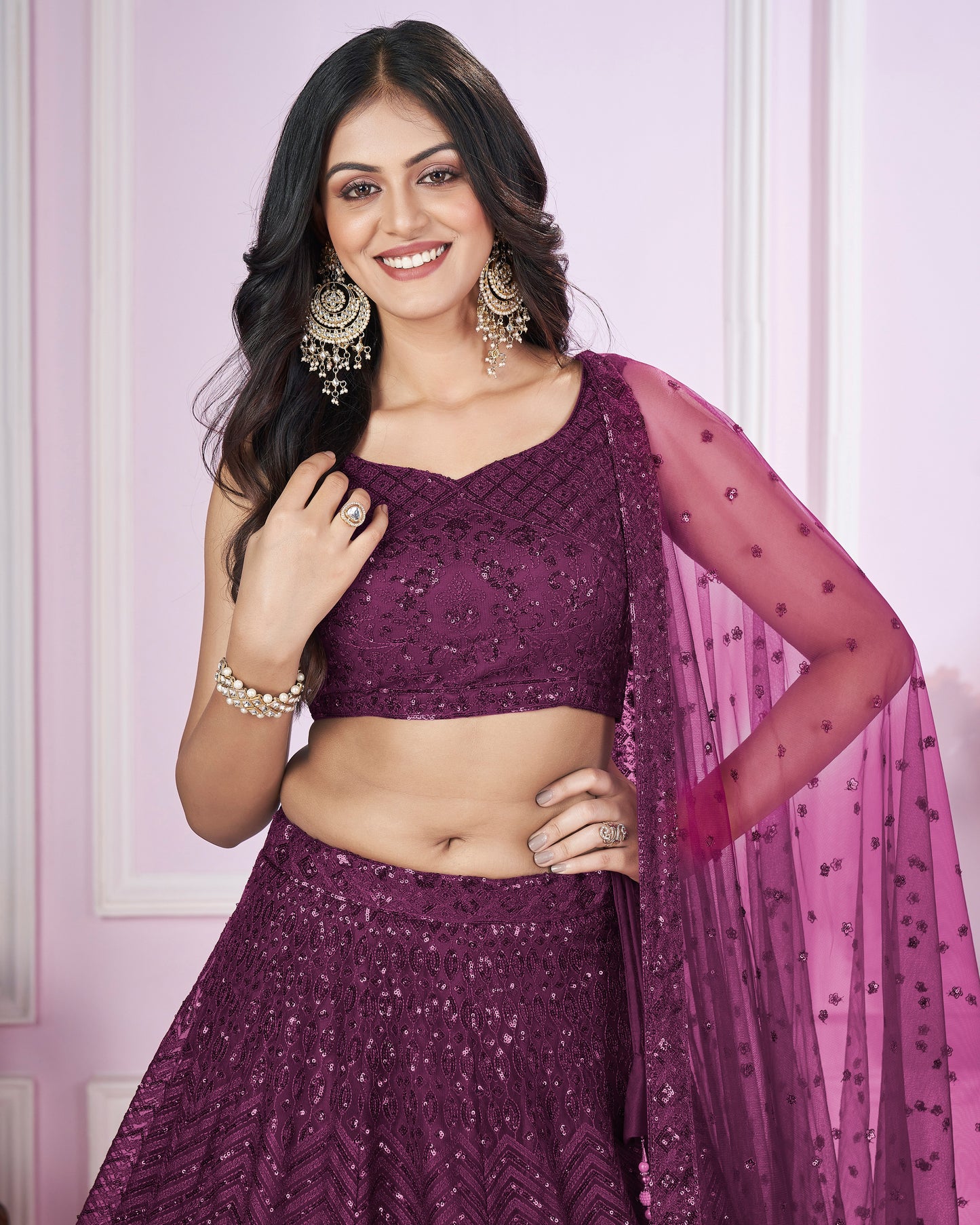 Woman wearing a purple traditional outfit with a matching dupatta against a light pink background