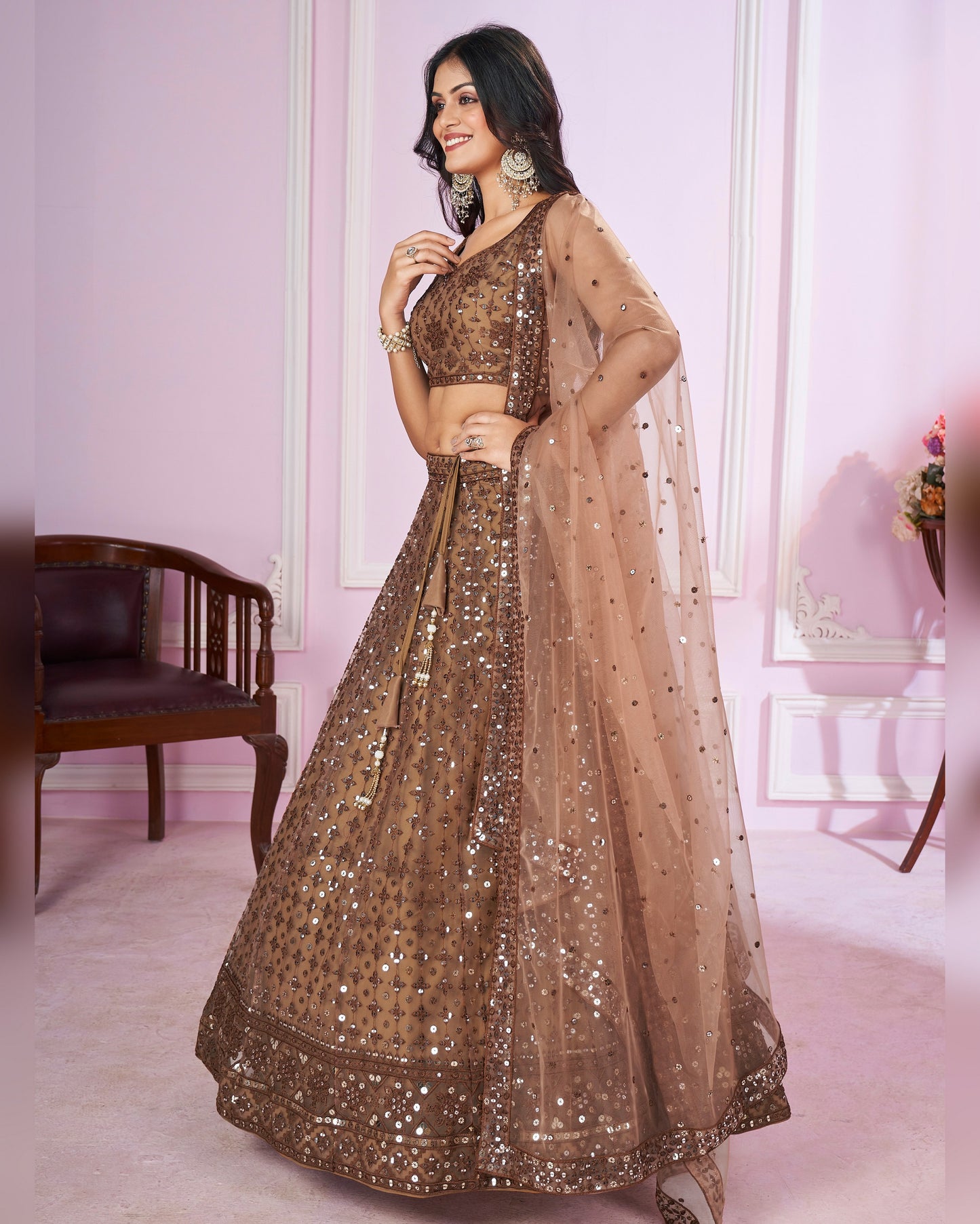 Woman wearing a brown embroidered lehenga in a room with pink walls and a chair.
