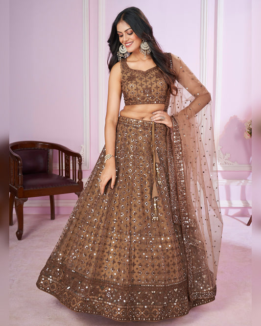 Woman wearing a brown traditional outfit with a matching dupatta in a pink room.