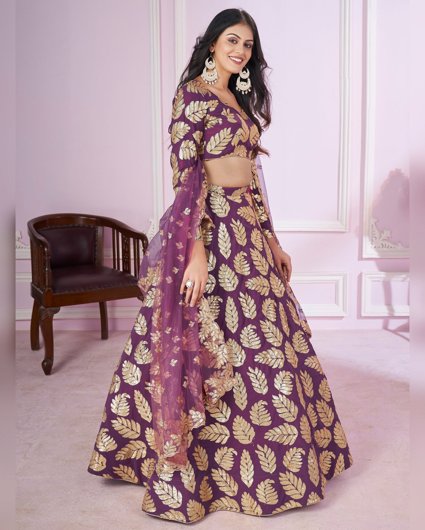 Woman wearing a purple and gold traditional outfit with a leaf pattern in a room.