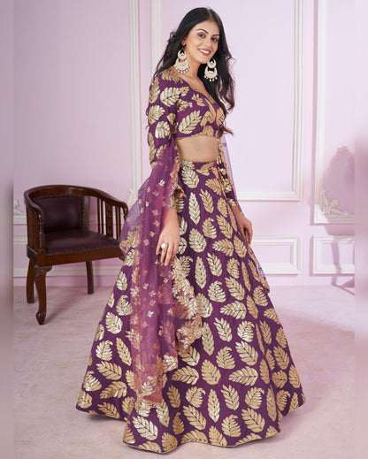 Woman wearing a purple and gold traditional outfit with a leaf pattern in a room.