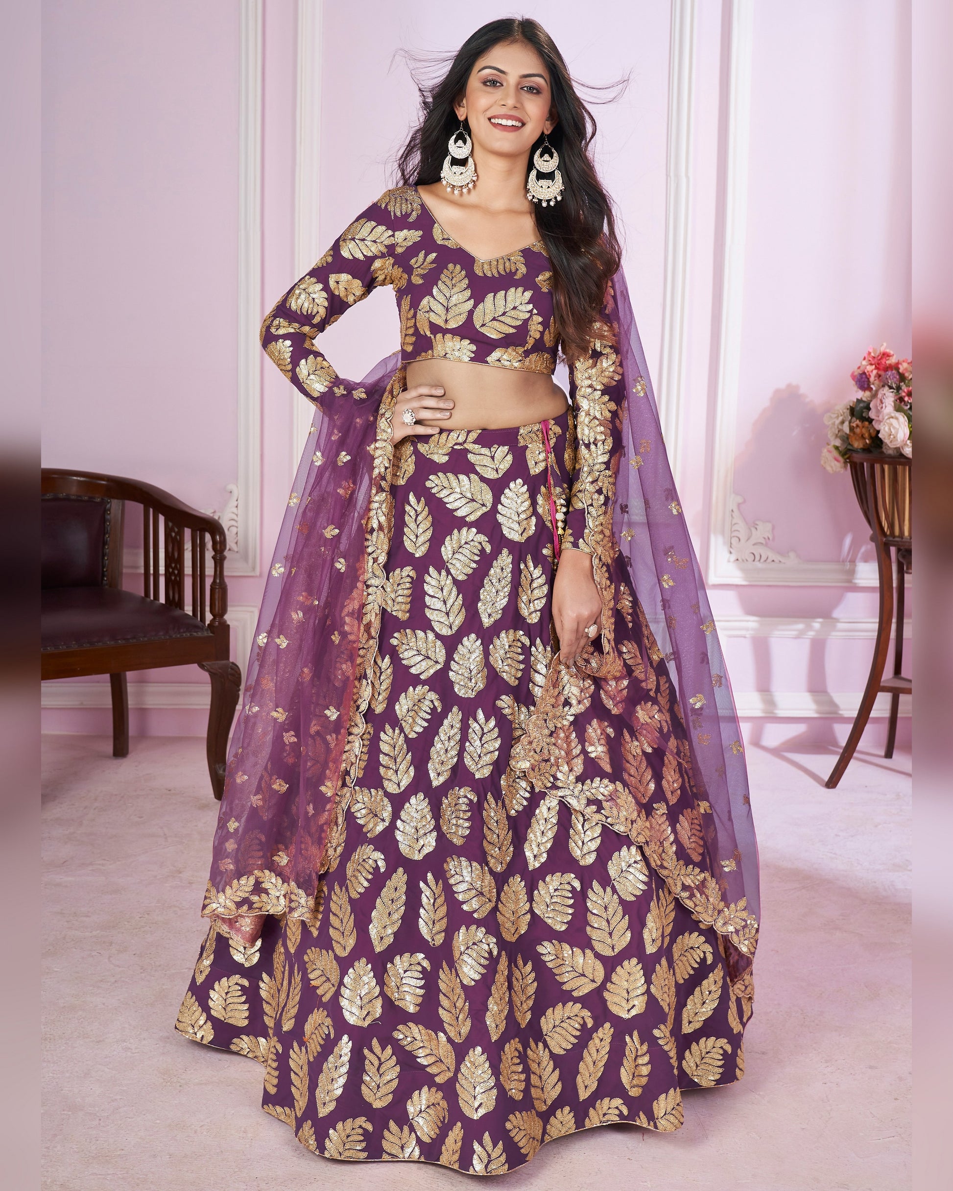 Woman wearing a purple and gold traditional outfit with a matching dupatta in a room.