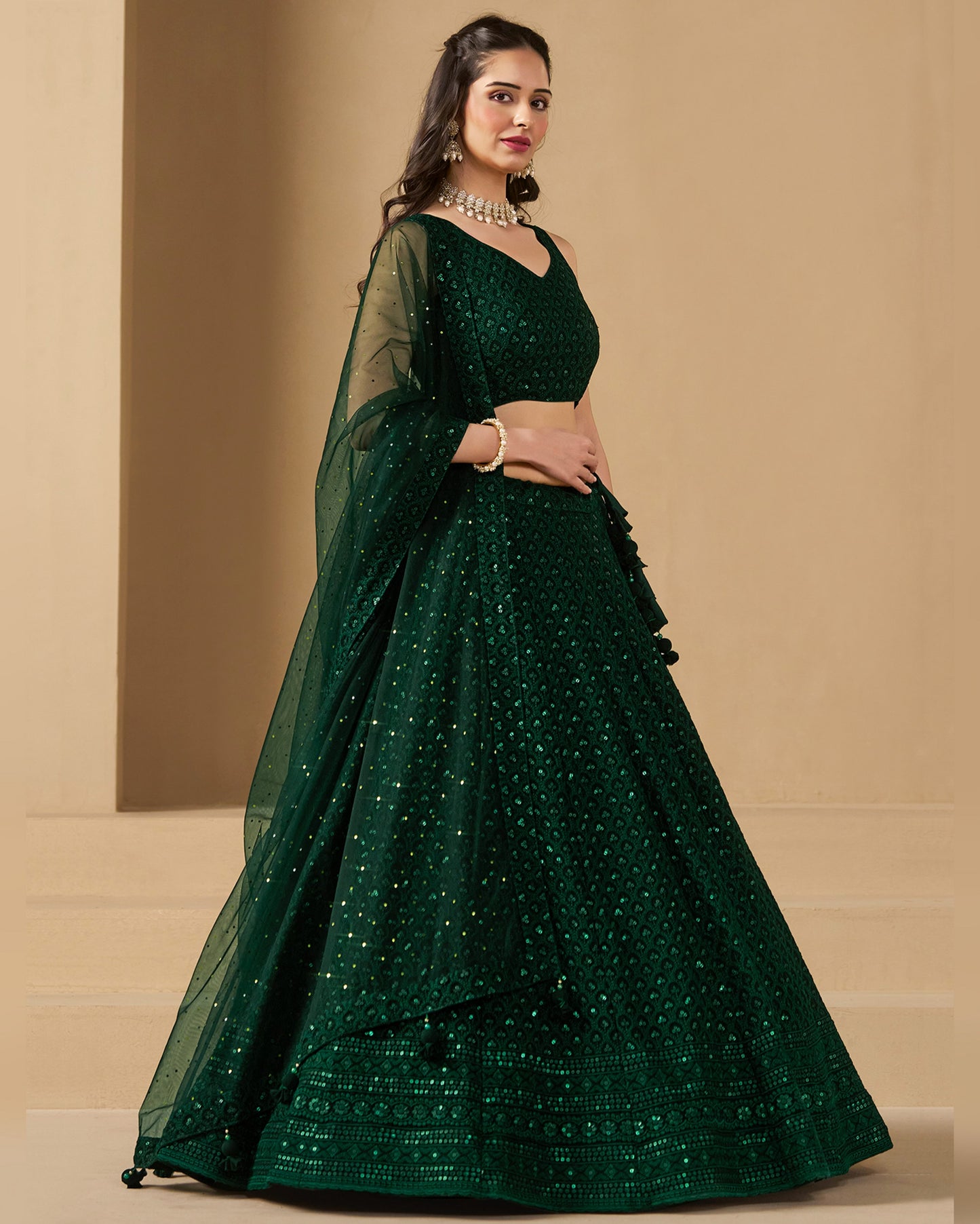 Woman wearing a green embroidered lehenga with a matching blouse on a beige background