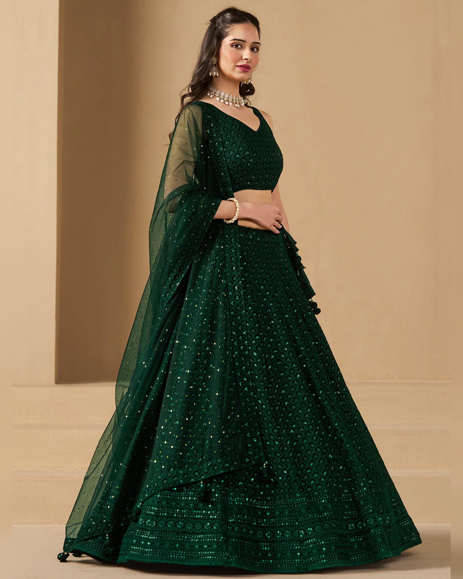 Woman wearing a green embroidered lehenga with a matching blouse on a beige background