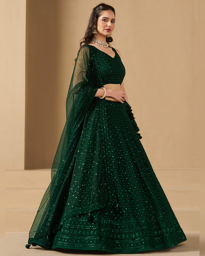 Woman wearing a green embroidered lehenga with a matching blouse on a beige background