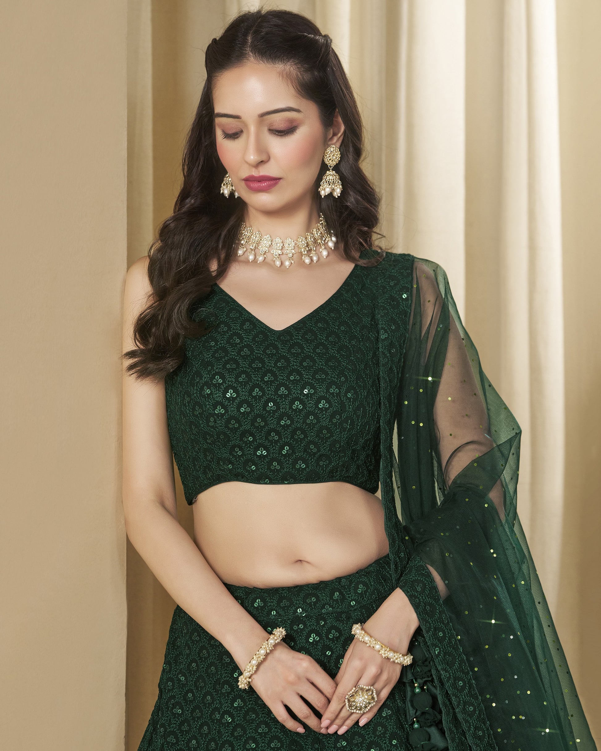 Woman wearing a green embroidered outfit with jewelry against a beige curtain background