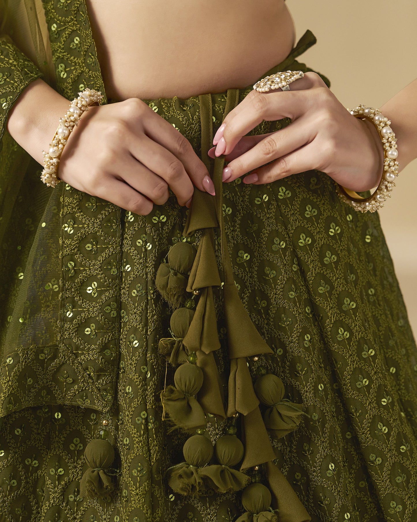 Close-up of a person wearing a green embroidered garment with tassels and jewelry.