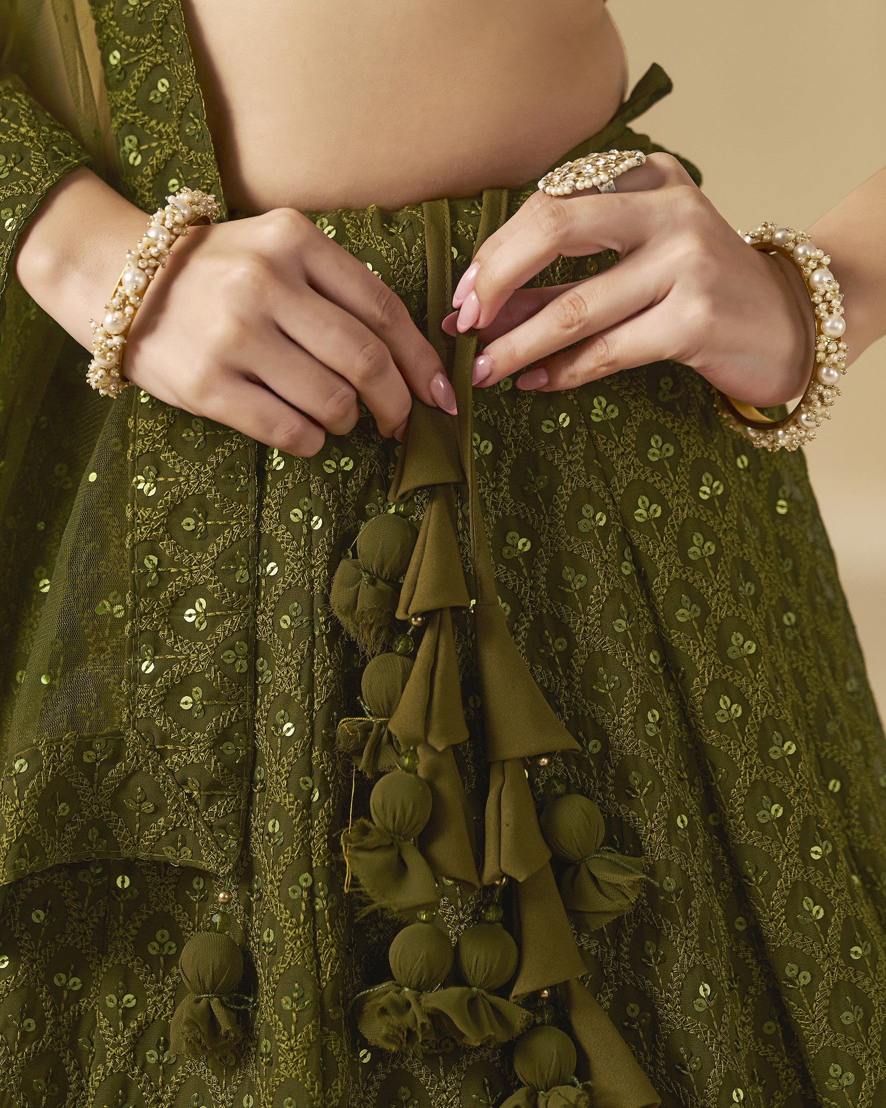 Close-up of a person wearing a green embroidered garment with tassels and jewelry.