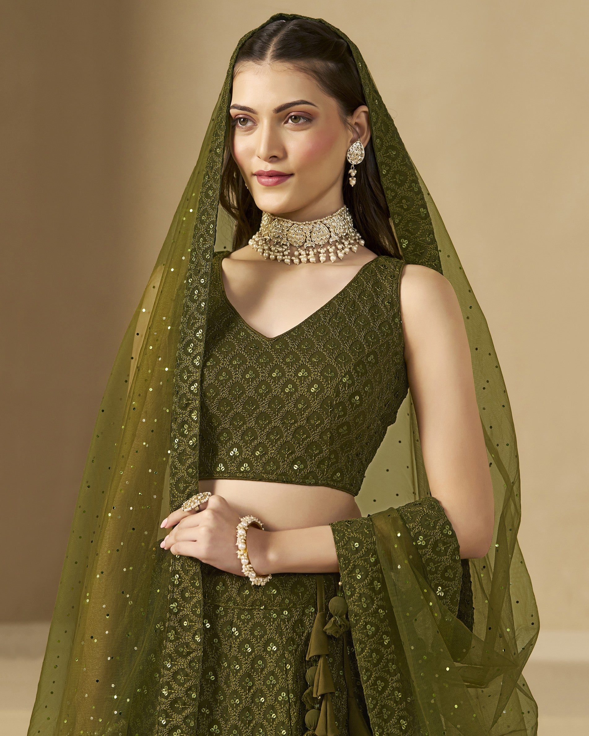 Woman wearing a green embroidered saree with a matching blouse and dupatta on a beige background