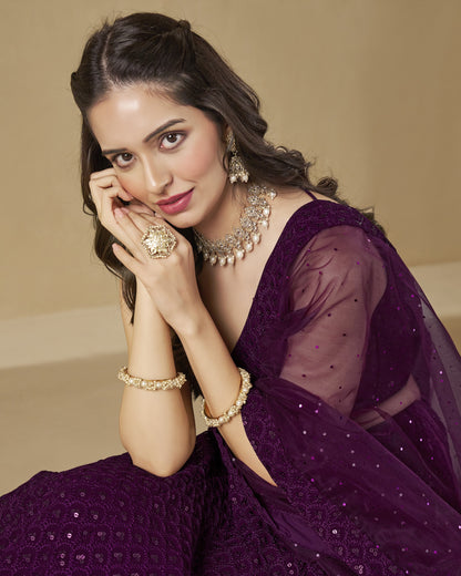 Woman in a purple saree with jewelry against a beige background