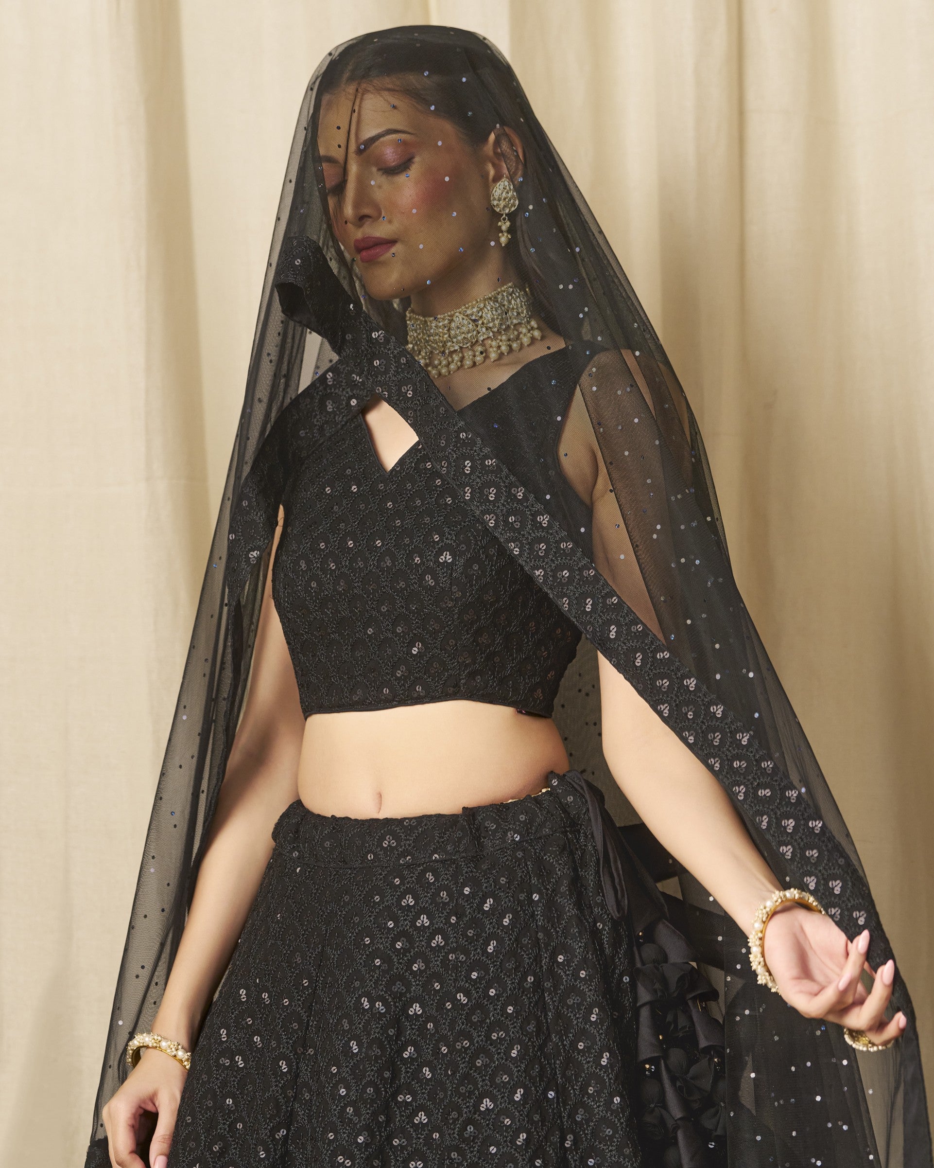 Woman wearing a black traditional outfit with a sheer dupatta against a beige curtain background